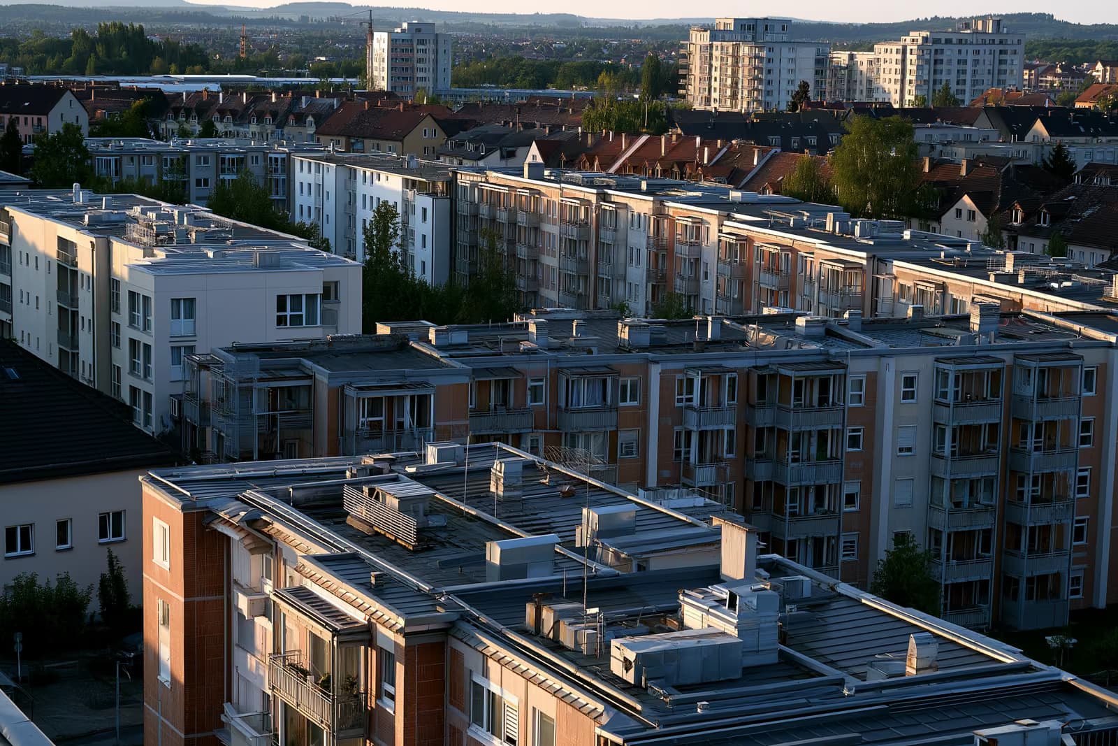 Střechy a větrací otvory topení na bytových domech v německém městě za teplého odpoledního světla.