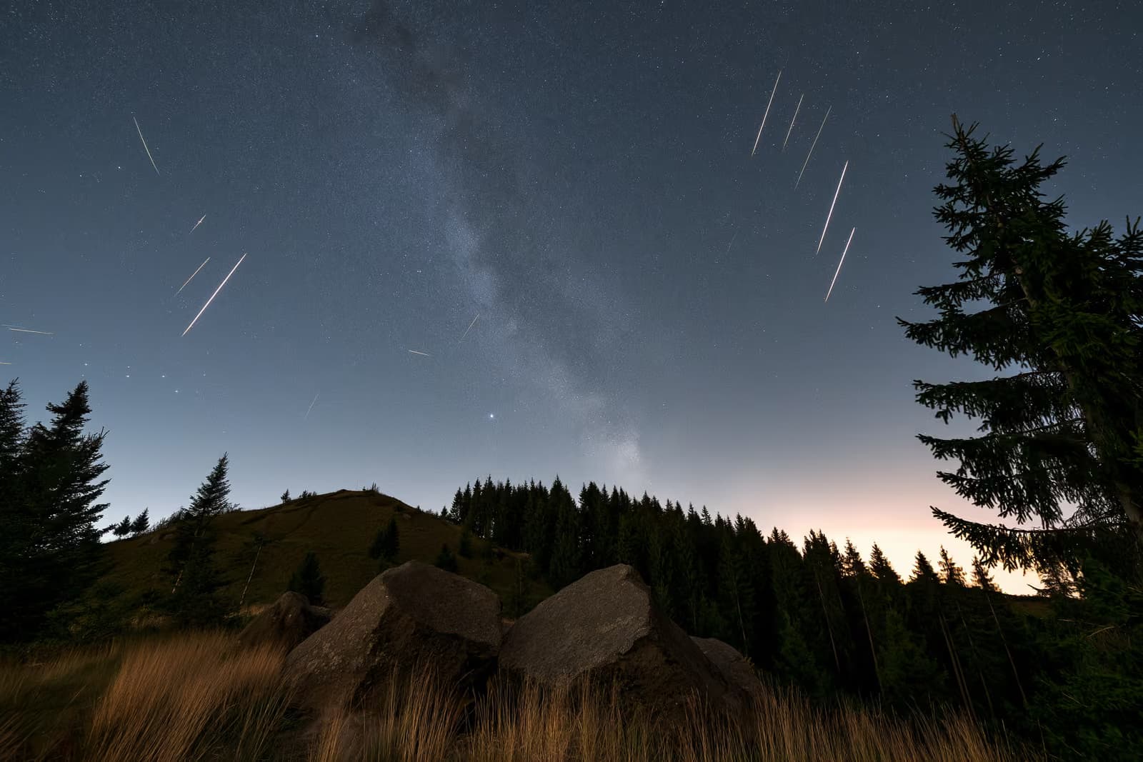 Noční obloha nad temnou německou krajinou s meteorickými pruhy a slabým pásem hvězd nad hlavou.
